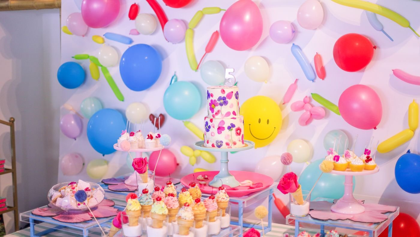 Colourful birthday party dessert table with cake, cupcakes and a balloon backdrop