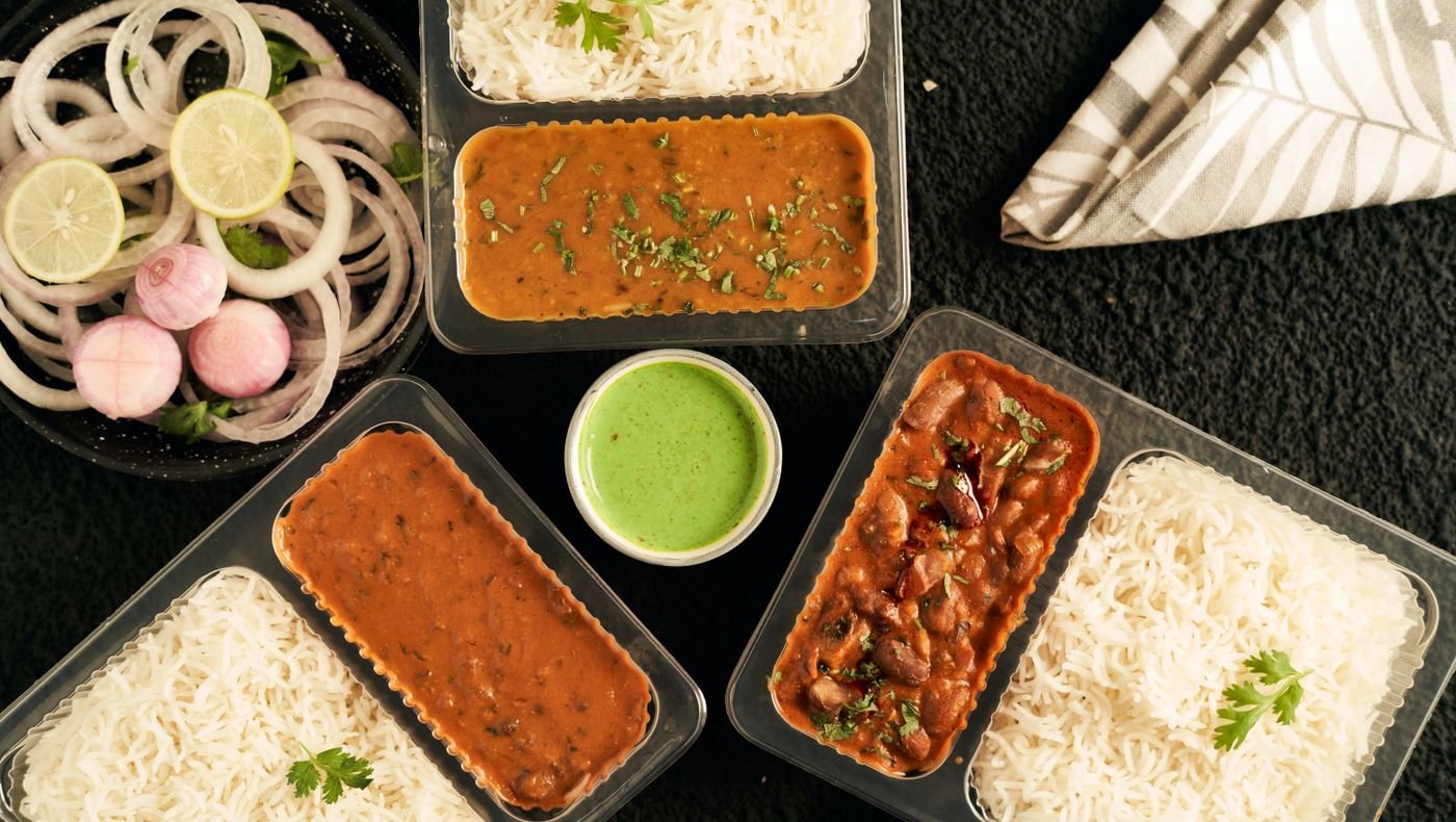 Packed daily meal boxes of dal, rajma curry and basmati rice with chutney and onion salad