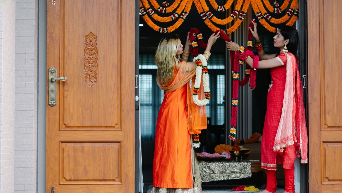Women hanging marigold garlands over a home doorway for a Griha Pravesh house warming